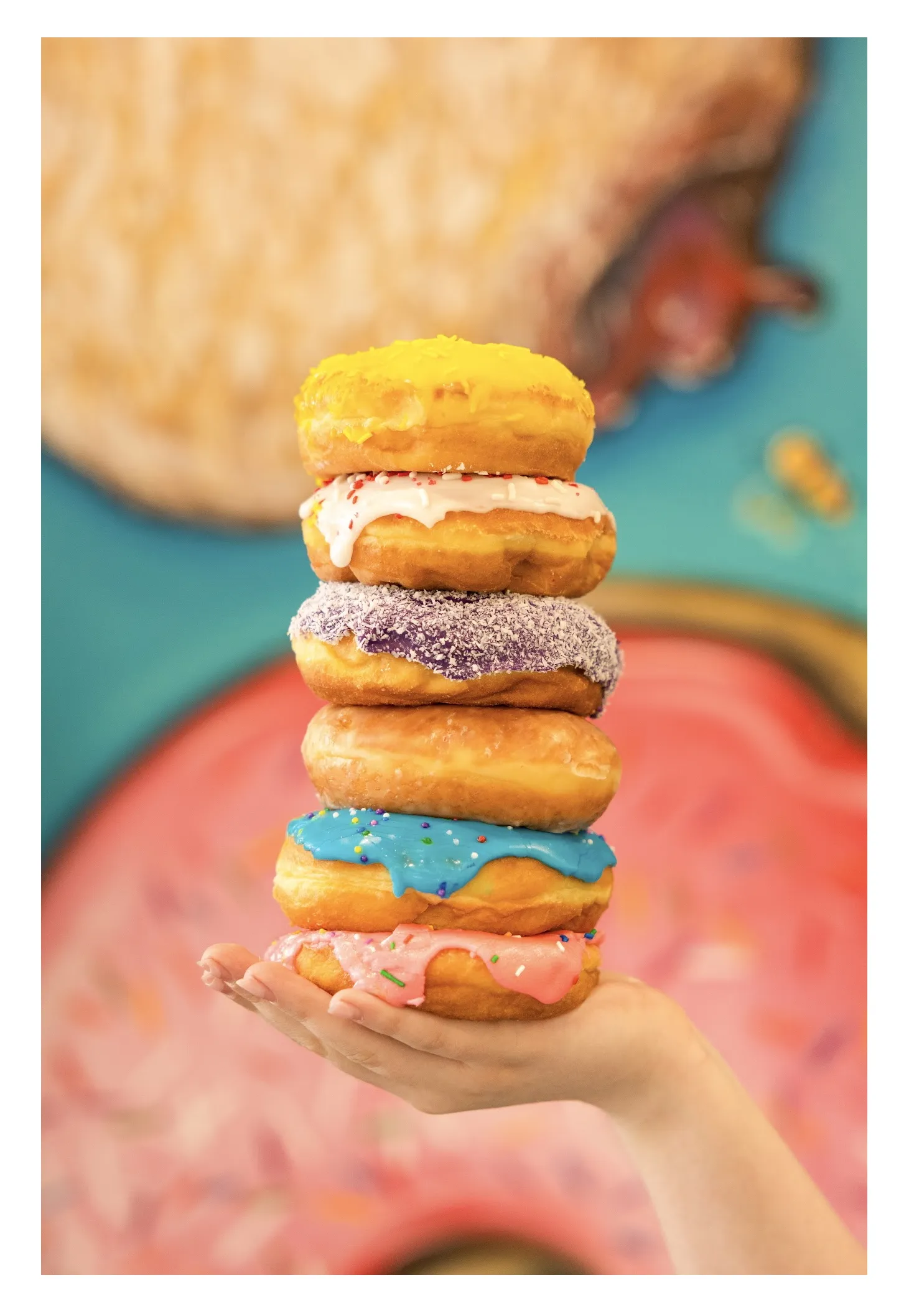 A tall stack of assorted Hive Donut Hut donuts, frosted in pink, chocolate and vanilla and finished with sprinkles.